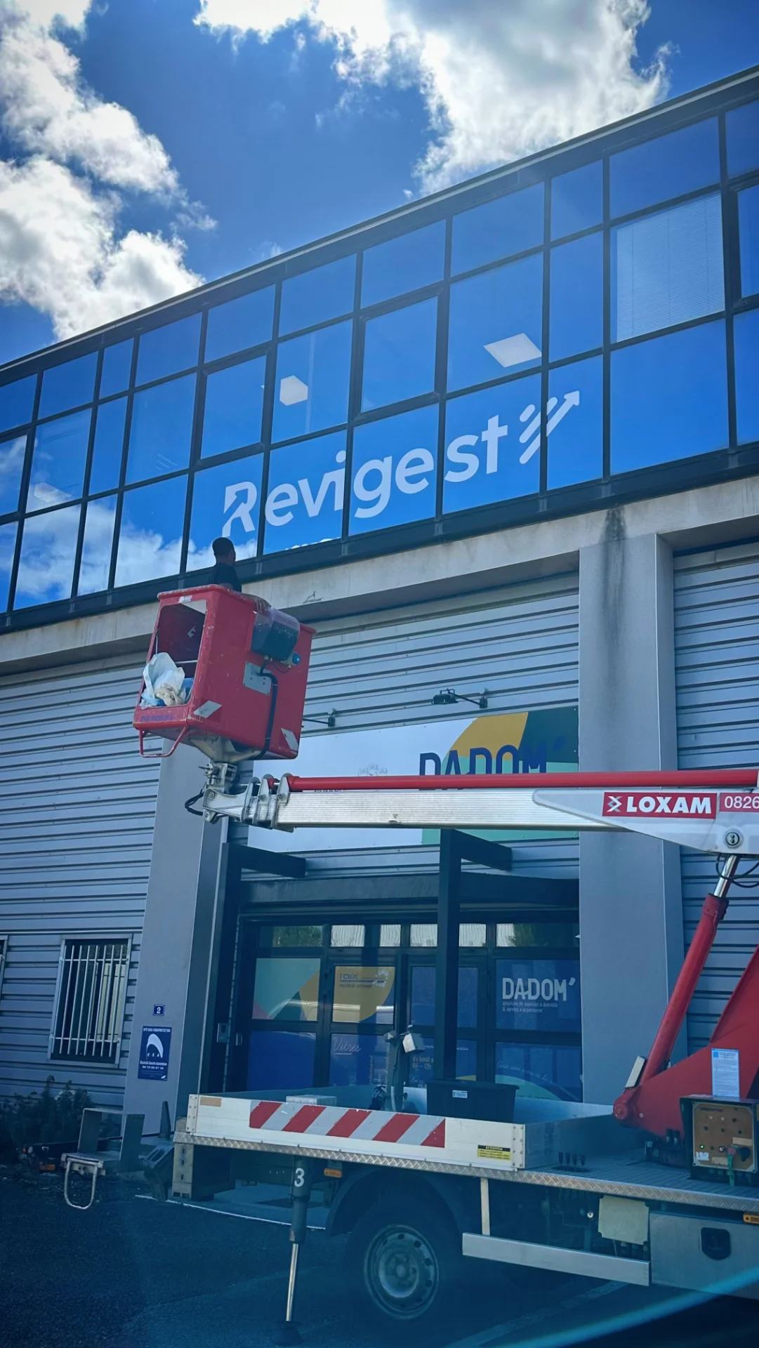 Pose en hauteur d’un vinyle adhésif personnalisé représentant le logo Revigest. Cette installation sur mesure assure une visibilité optimale de l’identité de l’entreprise tout en apportant une finition propre, professionnelle et durable aux locaux.