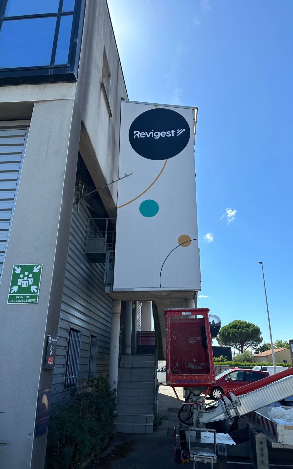 Pose en hauteur d’un adhésif imprimé représentant le logo Revigest. Cette installation sur mesure assure une visibilité optimale de l’identité de l’entreprise tout en apportant une finition propre, professionnelle et durable aux locaux.