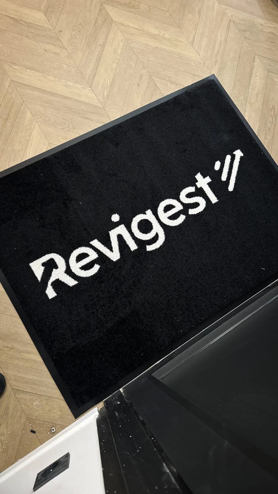 Conception et réalisation d’un tapis personnalisé haut de gamme pour Revigest. Ce support de communication sur mesure reprend fidèlement l’identité visuelle, le logo et les couleurs de la marque afin d’offrir un rendu professionnel, élégant et durable. Installé dans un espace d’accueil, un commerce ou lors d’un événement, ce tapis personnalisé renforce la visibilité de l’entreprise tout en apportant une finition soignée et premium à l’aménagement.